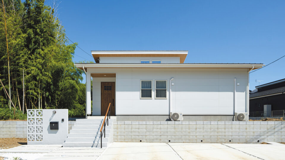 2階建のように見える勾配天井の屋根部分が顔をのぞかせているファサード。
真っ白な外壁を玄関ドアや軒天などの木目で引き締め、自然に映える佇まいに。
花ブロックをあしらった門柱はリゾート感を演出。