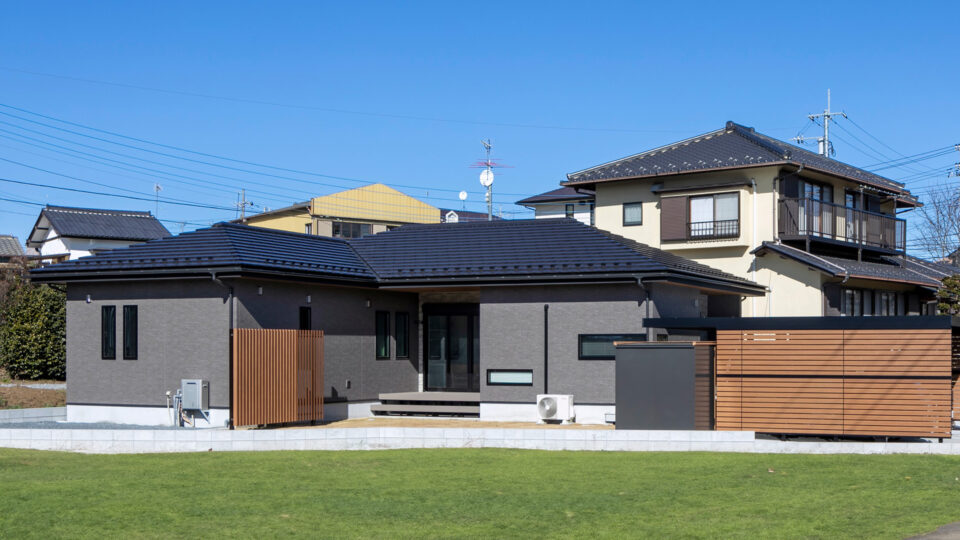 コの字型の平屋は、変形地を活かして必要な空間をうまく配置。
木製のフェンスが温もりを添え、落ち着いた雰囲気のブラウングレーの外壁と黒い窓枠の外観。